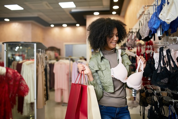 Young smiling attractive african american woman choosing right bra size in lingerie store black