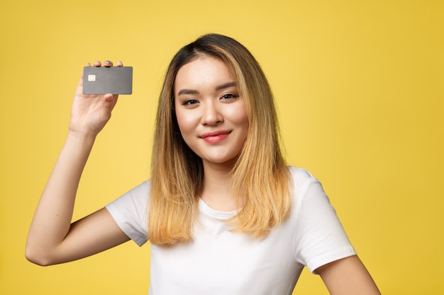 Photo young smiling beautiful asian woman presenting credit card in hand showing trust