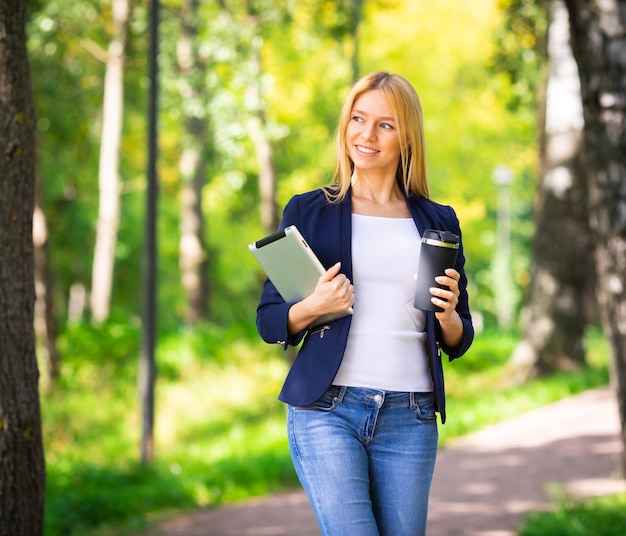 Young smiling beautiful woman in park with tablet gadget and wireless headphones enjoying green energy concept remote work