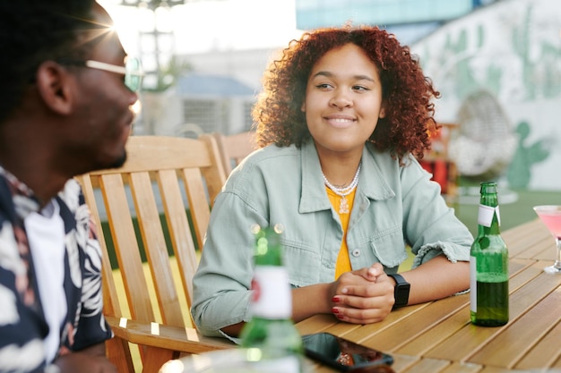 Young smiling black woman looking at her boyfriend during chat in cafe