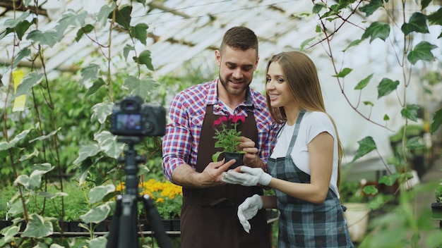 Young smiling blogger couple gardeners in apron holding flower talking and recording video blog