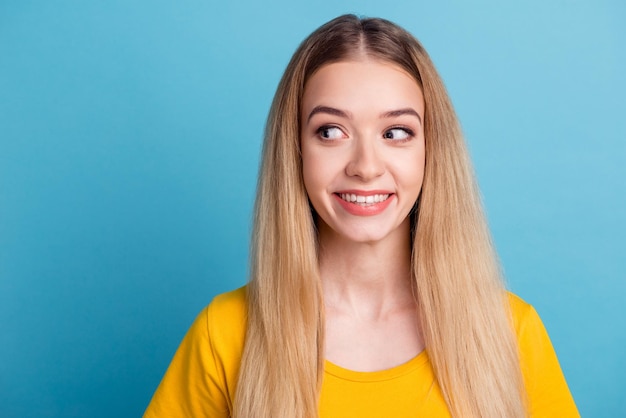 Young smiling blond girl with perfect teeth standing relaxed against blue background in casual clothes