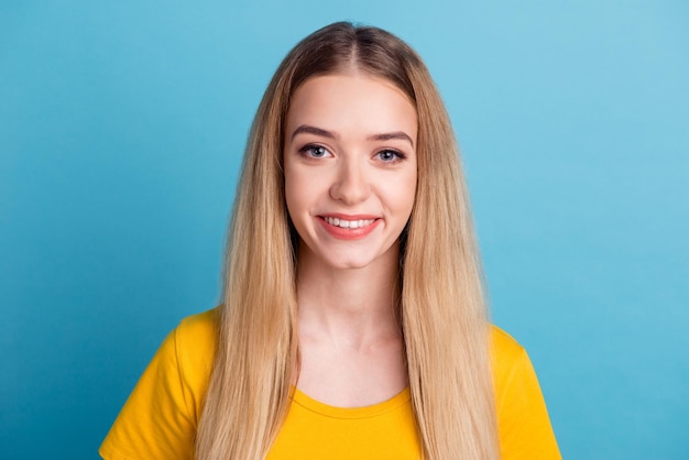 Young smiling blond girl with perfect teeth staring at camera relaxed against blue background in casual clothes