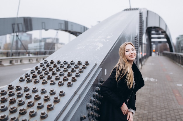 Young smiling blondie business woman near bridge. Walking along european city