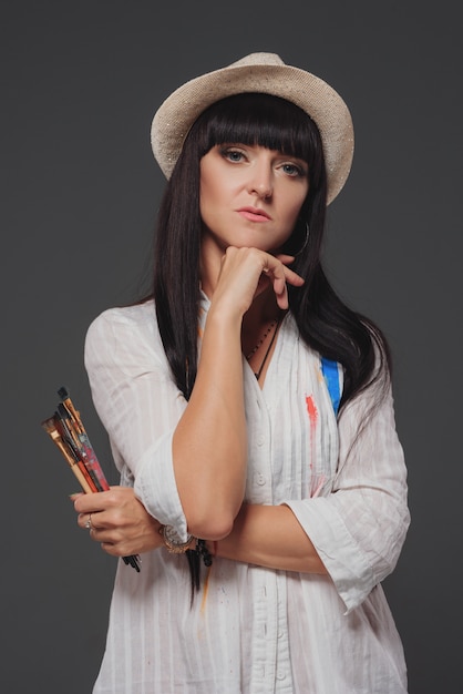 A young smiling brunette woman artist in her Studio is holding a brush.