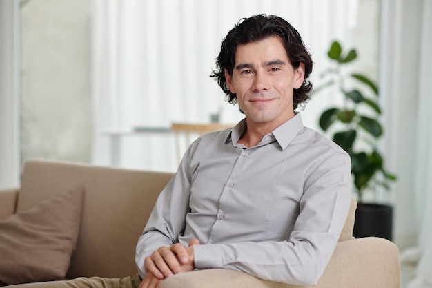 Young smiling businessman blogger or psychologist sitting on couch