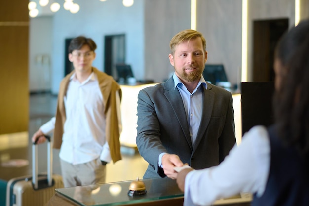 Young smiling businessman giving keycard back to female receptionist by counter