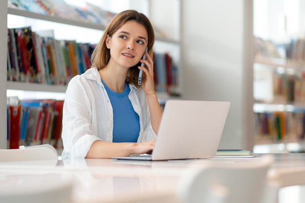 Young smiling businesswoman talking on mobile phone using laptop working online