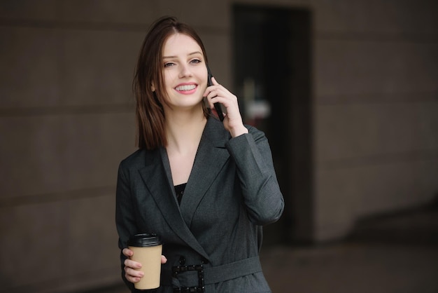 Young smiling businesswoman with coffee talking on the phone on the street