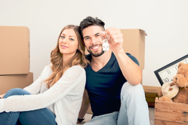 Young smiling couple holding their new house keys, real estate and relocation concept