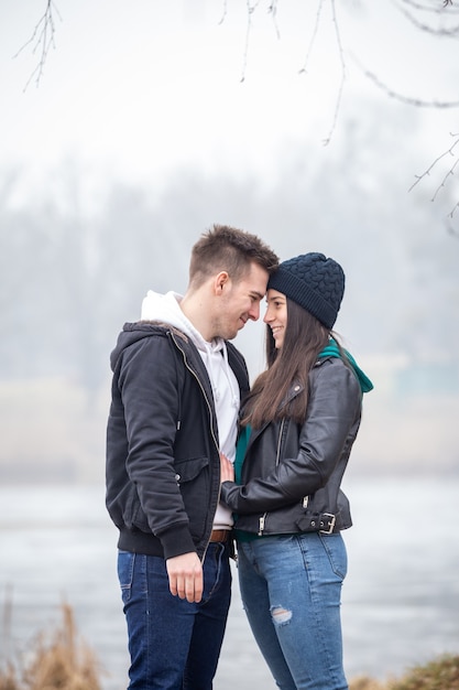 Young smiling couple standing on shore of Lake Gebart Zalaegerszeg Hungary on a foggy winter day