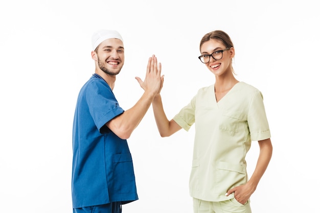 Young smiling doctor with phonendoscope on neck and pretty nurse in eyeglasses and uniform giving five gesture to each other while happily 