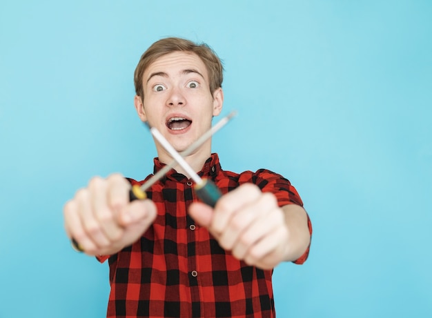 Young smiling emotional male teenager in red shirt on blue background with screwdriver