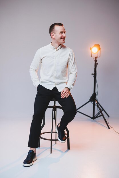 A young smiling European man in a shirt and black pants sits on a chair and smiles at the camera A stylish man in casual clothes