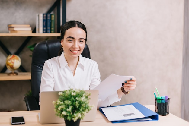 Young smiling female holds documents in her hands and looks into camera in office