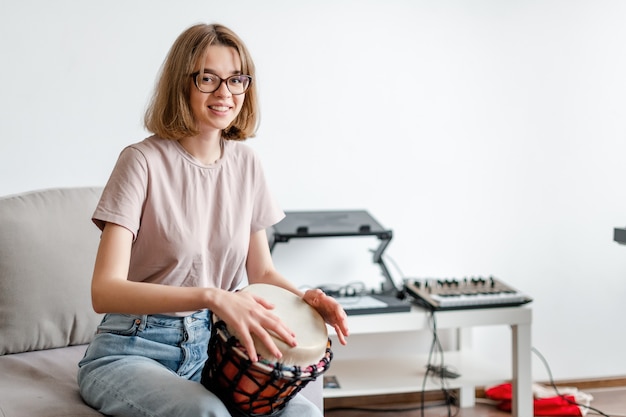 Young smiling female learning how to play djembe at home copyspace