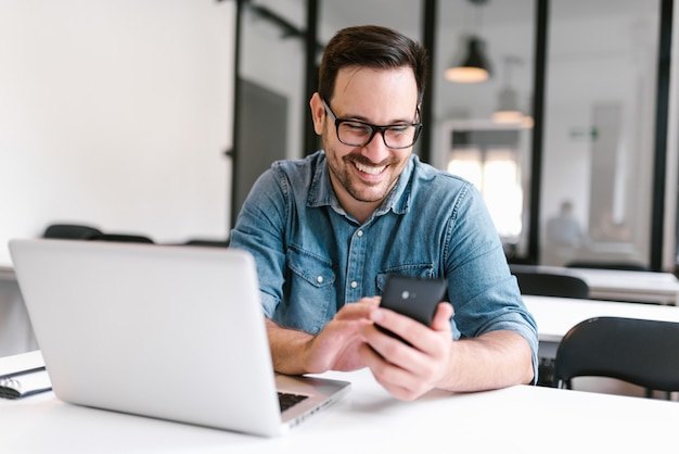 Young smiling freelancer reading message on the smartphone.