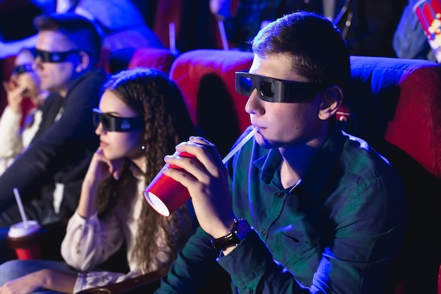 Young smiling friends in 3d glasses eating popcorn and watching movie in cinema