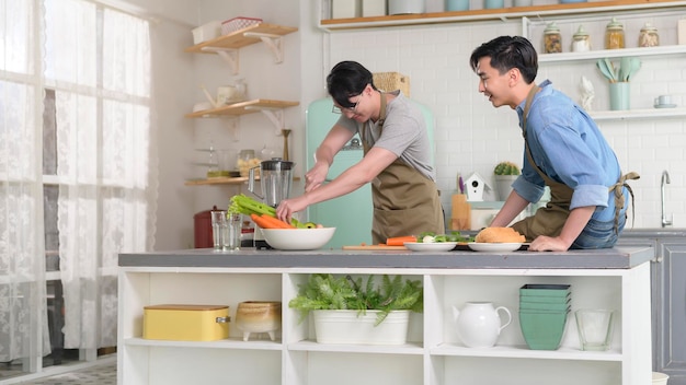 Young smiling gay couple cooking together in the kitchen at home LGBTQ and diversity concept