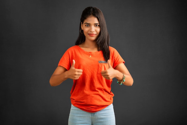 Young smiling girl showing ok sign or thumbs up on a grey background