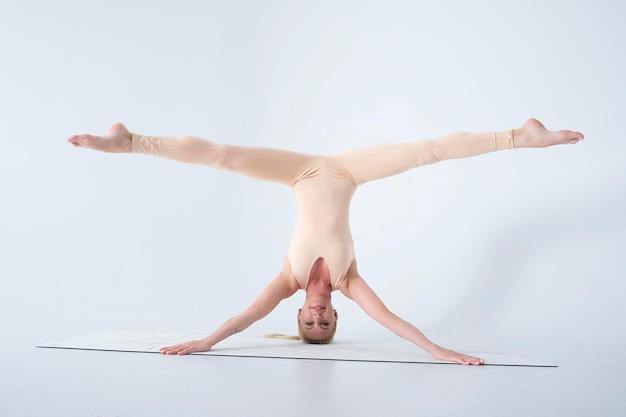 Young smiling girl shows yoga asanas standing on her head and spreading her legs in a cross twine