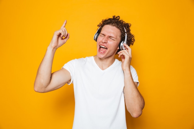 Young smiling guy with curly hair listening to music via headphones and singing