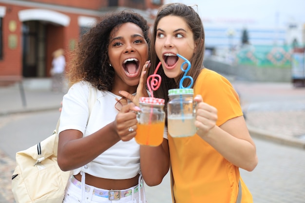 Young smiling hipster women in summer clothes posing on street.Female showing positive face emotions.