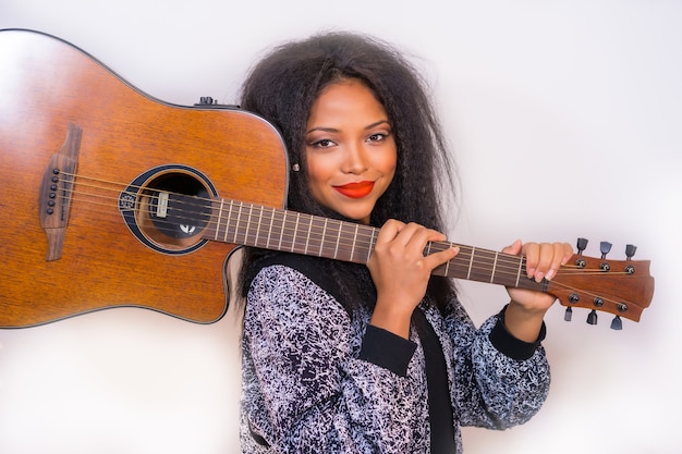 of a young smiling Hispanic female posing at the camera holding a guitar on her shoulder on white