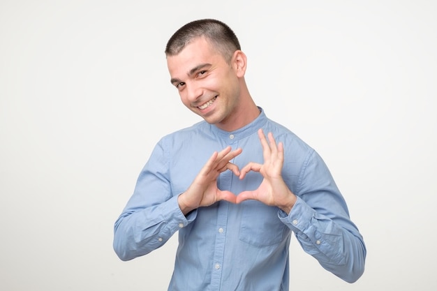 Young smiling hispanic man in blue shirt showing heart sign