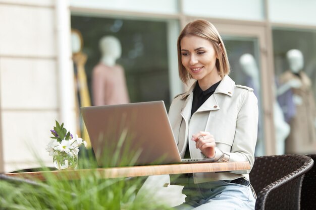 Young smiling lady with laptop sits in an outdoor cafe Lifestyle remote work or education