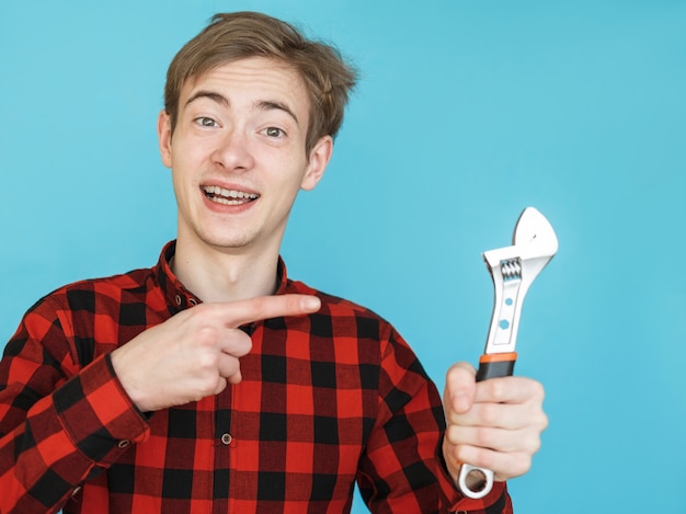 Young smiling male teenager in red shirt on blue background with tools wrench