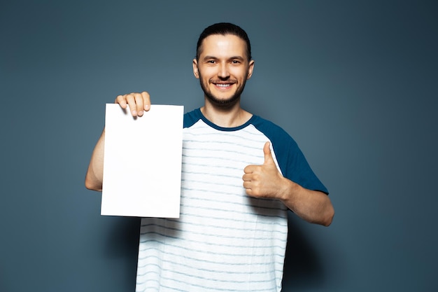 Young smiling man holding empty board showing thumbs up on blue background