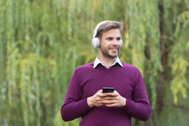 Young smiling man listen music in headphones and chating on phone outdoor