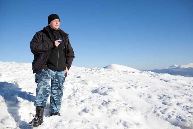 Young smiling man photographer in winter clothing drinking tea from thermos