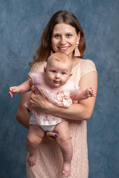 A young smiling mother in a light dress holds a newborn daughter in her arms