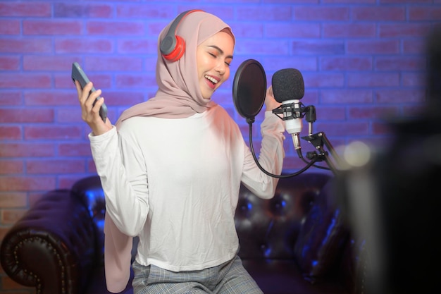 A young smiling muslim female singer wearing headphones with a microphone while recording song