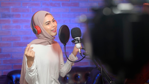 A young smiling muslim female singer wearing headphones with a microphone while recording song