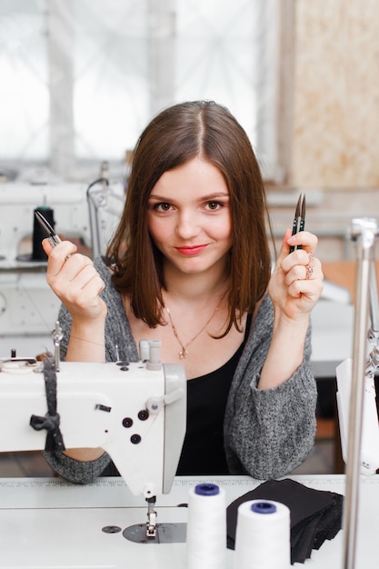 Young smiling seamstress posing with scissors.