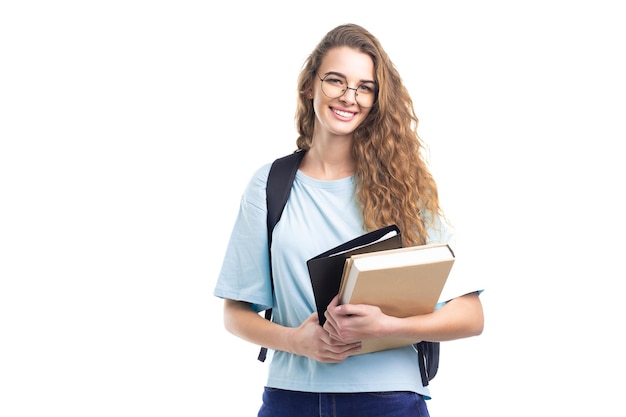 Young smiling student girl holds books while looking at camera over white background education