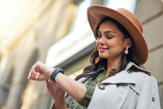 Young smiling stylish woman wearing grey coat and hat checking the time while standing on