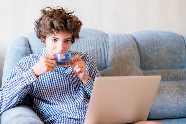 Young smiling teenager with long hair studying at home using laptop sitting on  a sofa