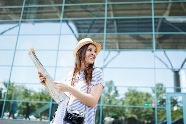 Young smiling traveler tourist woman with retro vintage photo camera holds paper map looking aside at international airport