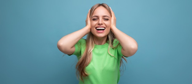 Young smiling woman in casual attire covered her ears from a loud sound on a blue isolated