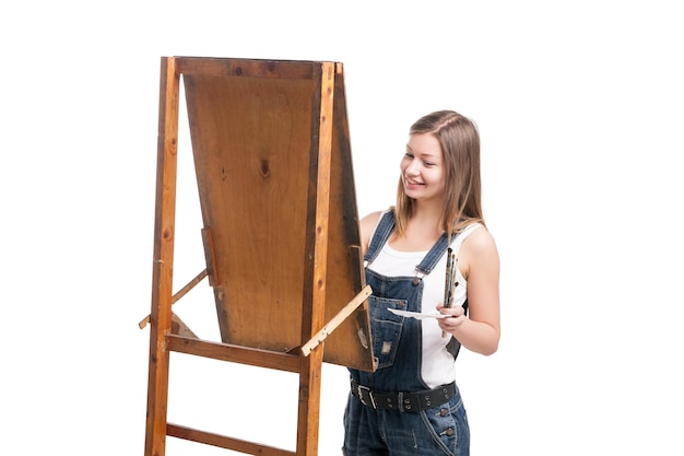 Young smiling woman draws with paintbrush  easel isolated against white background