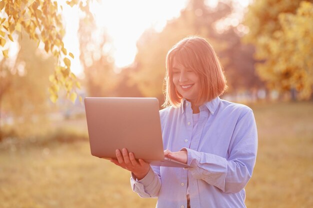 Young smiling woman in green park with laptop