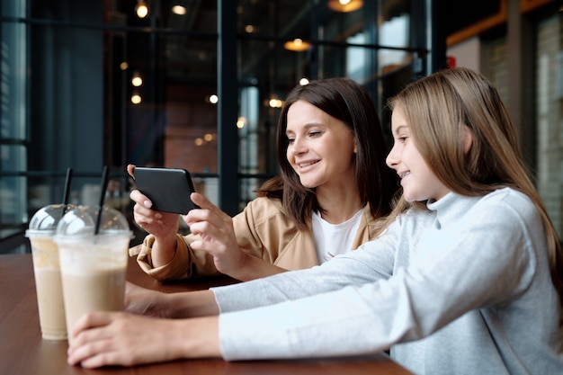 Young smiling woman and her cute daughter sitting in cafe