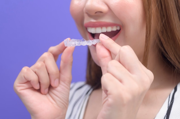 A young smiling woman holding invisalign braces in studio, dental healthcare and Orthodontic concept.