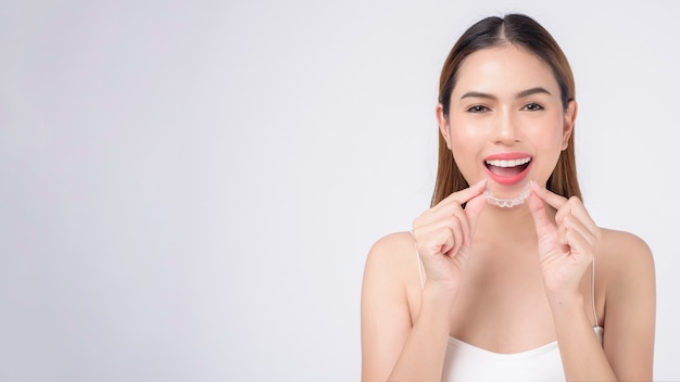 Young smiling woman holding invisalign braces in studio, dental healthcare and Orthodontic concept