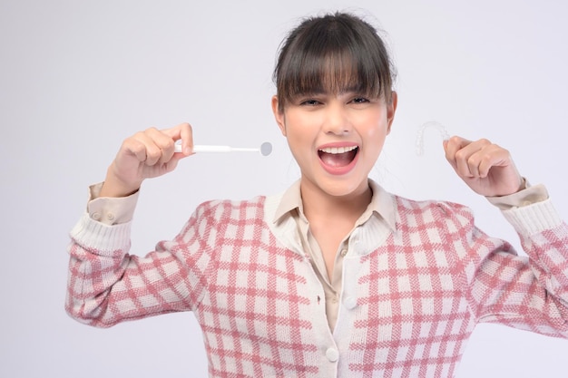 A young smiling woman holding invisalign braces over white background studio