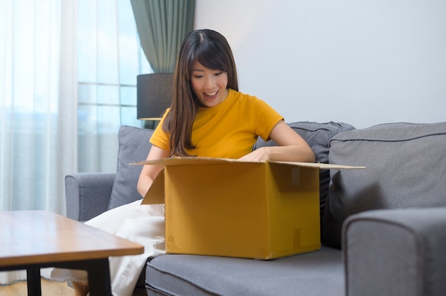 A young smiling woman opening cardboard box in living room at home